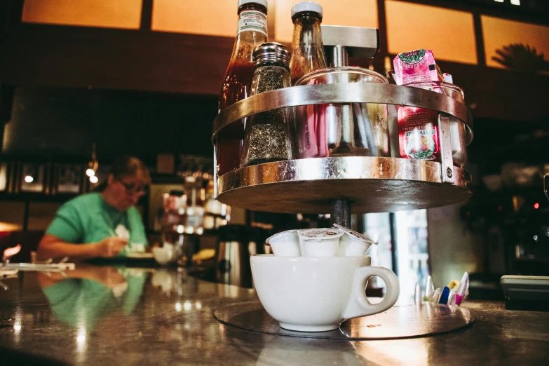 a cup of coffee sitting on top of a counter, by Joe Bowler, inside a bar, jenny seville, multiple stories, thumbnail