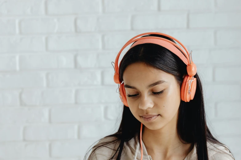 a woman wearing headphones looking at her cell phone, by Nicolette Macnamara, trending on pexels, hyperrealism, toned orange and pastel pink, sitting at a computer, wearing a headband, student