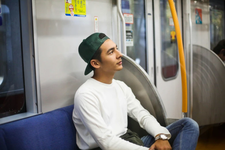 a young man wearing a hat and sitting on the subway