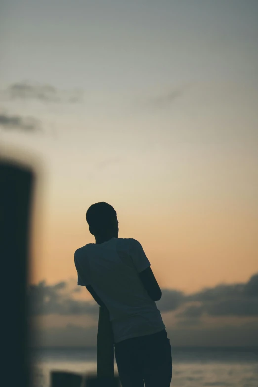 a man standing on top of a beach next to the ocean, a picture, unsplash, happening, girl watching sunset, human staring blankly ahead, sittin, low - angle shot from behind