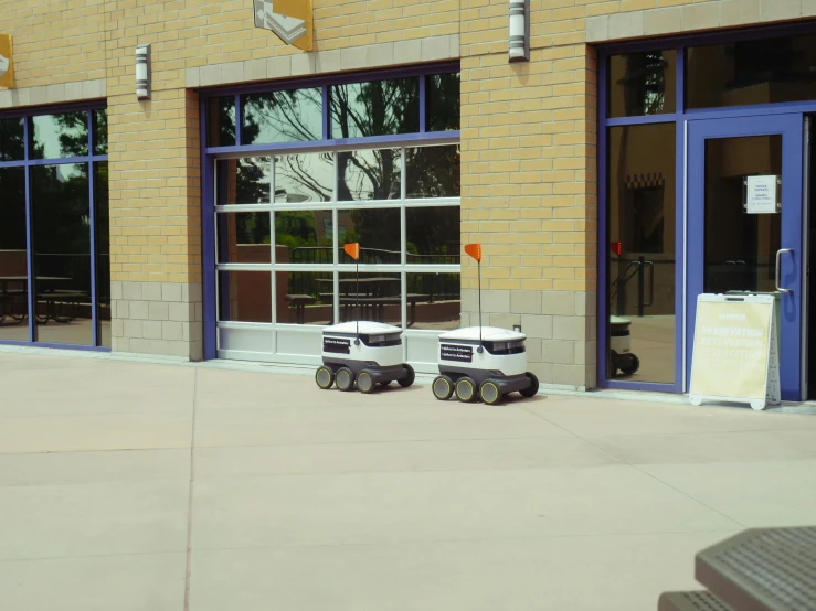 a toy truck is parked in front of a building, walking with a robot, school courtyard, promo image, they are close to each other