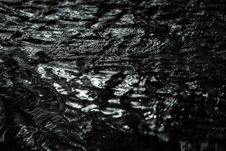 a black and white photo of a puddle of water, an album cover, inspired by Andreas Gursky, unsplash, lyrical abstraction, dark plastic, closeup 4k, mat black metal, shimmering iridescent water