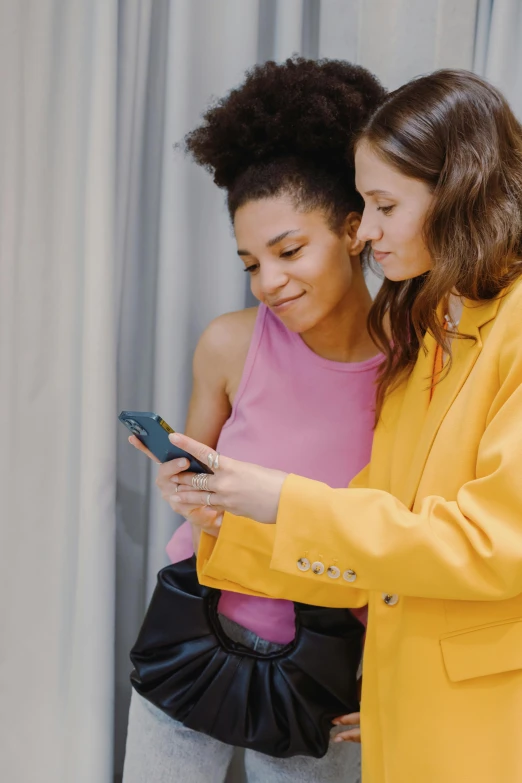 two women stand near one another looking at a cell phone