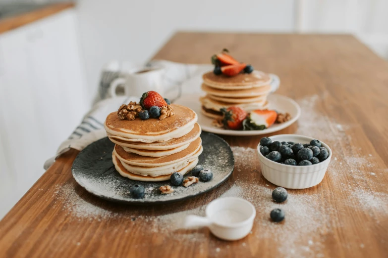 pancakes on two plates, covered with berries and blueberries