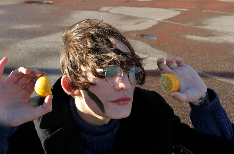 a young man holding two lemons in front of his face, an album cover, unsplash, cosplay, non binary model, 🐿🍸🍋, in the sun