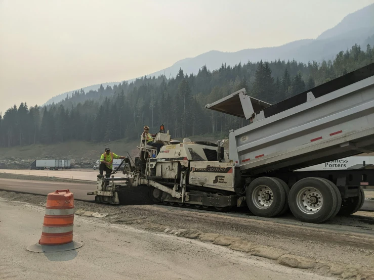 a dump truck that is sitting on the side of the road, by Brigette Barrager, reddit, paved roads, mountain in background, workers, british columbia