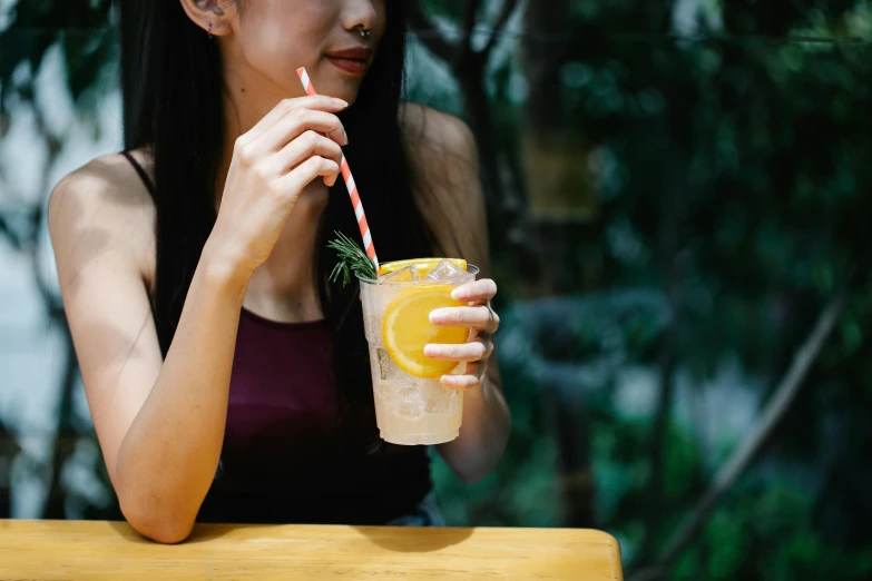 a woman sitting at a table drinking a drink, trending on pexels, straw, background image, manuka, asian female