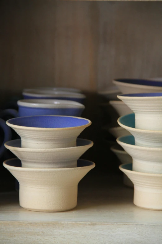 a close up of cups and saucers on a shelf, by Jessie Algie, dipped in polished blue ceramic, show from below, unfinished, wheels