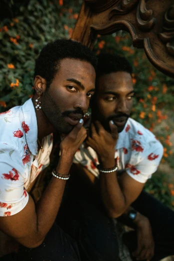 a couple of men sitting next to each other, an album cover, inspired by Gordon Parks, trending on unsplash, flower child, donald glover, thick mustache, beautiful gemini twins portrait
