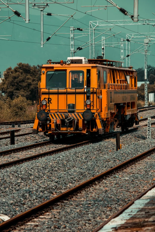a yellow train traveling down train tracks next to a forest, machinery and wires, square, high-quality photo, crypto