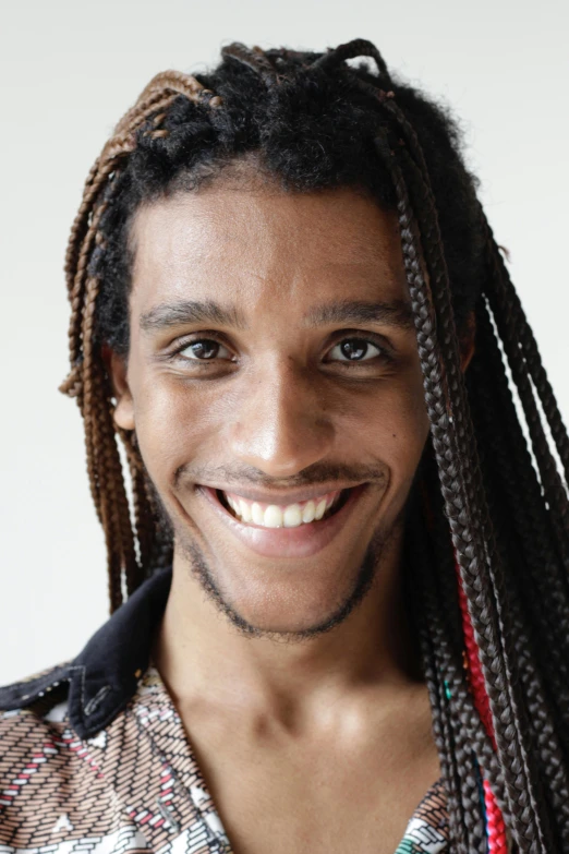 a smiling man with dreadlocks and a plaid shirt