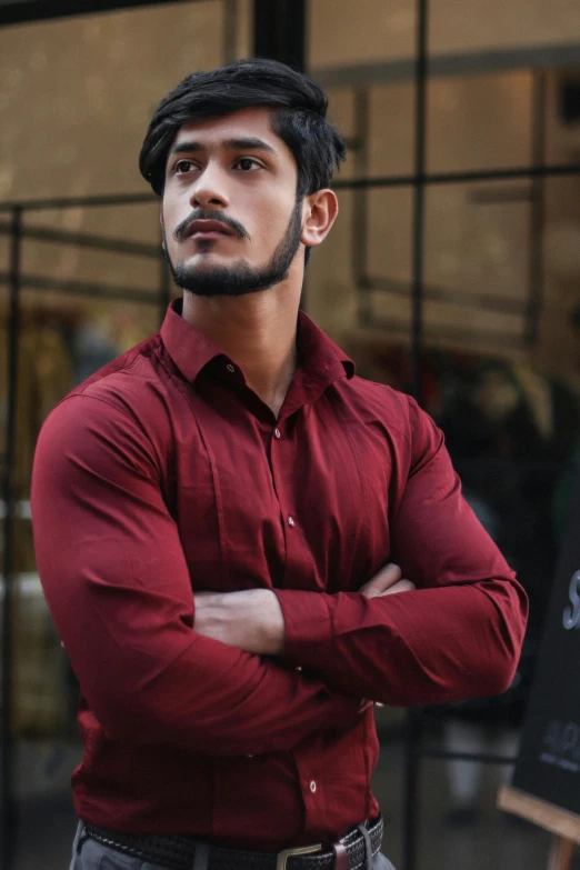 man in red shirt posing for picture while leaning his arms crossed