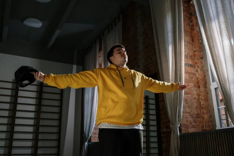 a man in a yellow hoodie standing in front of a window, pexels contest winner, classic dancer striking a pose, unreal engine cinematic smooth, ( ( theatrical ) ), standing in corner of room