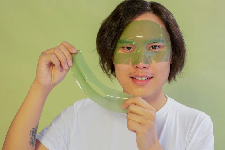 a man holding a banana in front of his face, an album cover, inspired by Nam Gye-u, green facemask, wearing translucent sheet, loputyn and matcha, silicone skin