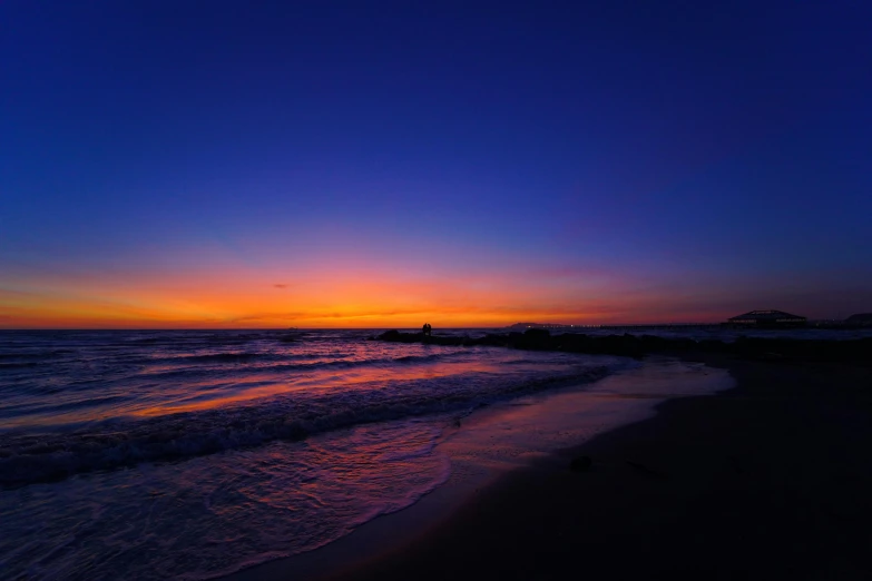 the sun is setting on a beach with waves lapping in front of it