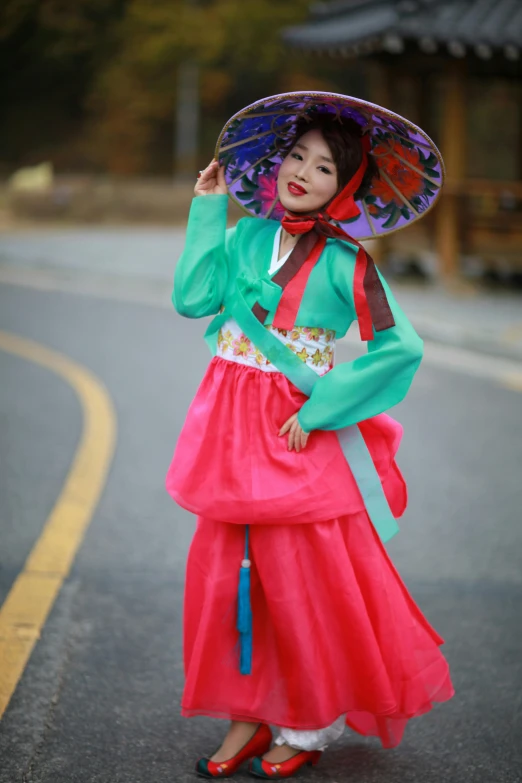 a woman in an asian style dress and hat poses on a road