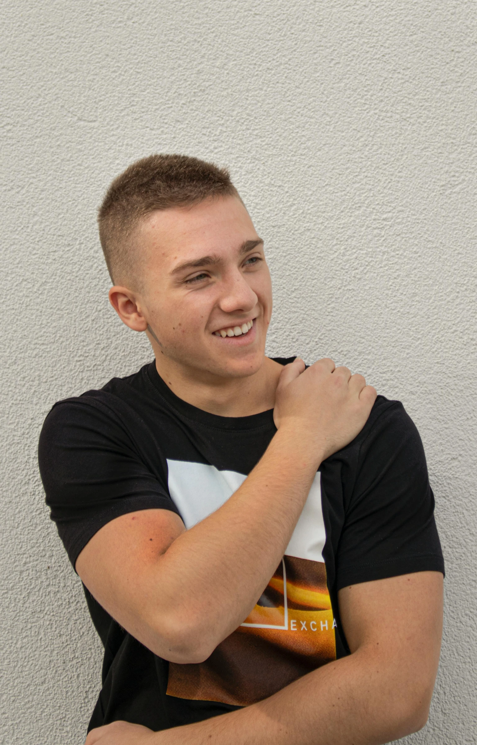 the man is leaning against a wall wearing a t - shirt