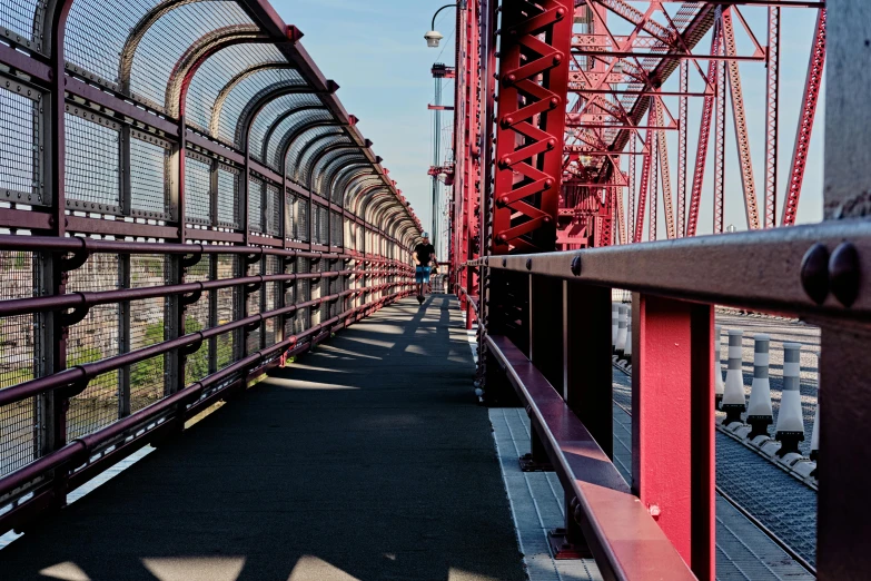 a person walking across a bridge on a sunny day, inspired by William Berra, pexels contest winner, red trusses, hell gate, reddish, high view