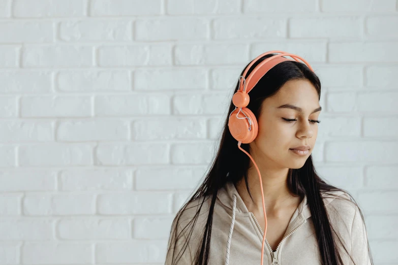 a woman wearing headphones standing in front of a brick wall, trending on pexels, toned orange and pastel pink, on a white background, subtle detailing, hyperrealistic teen