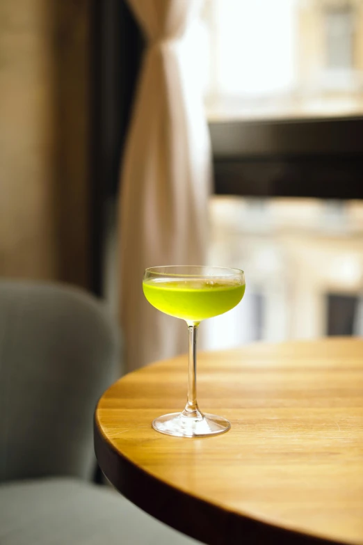 a glass filled with a green liquid sits on a round table