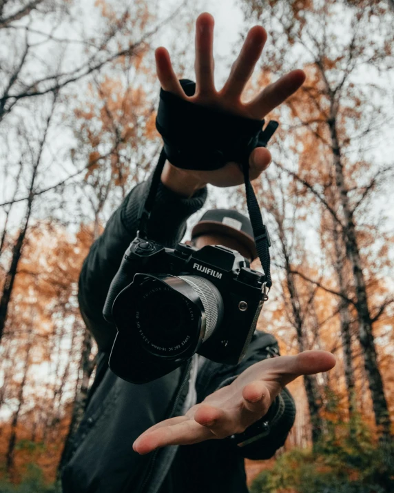 a person holding a camera in a forest, wave a hand at the camera, sony a7, fall season, low quality photo