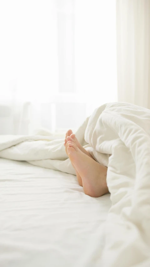 a person's feet sitting on a bed under a white blanket