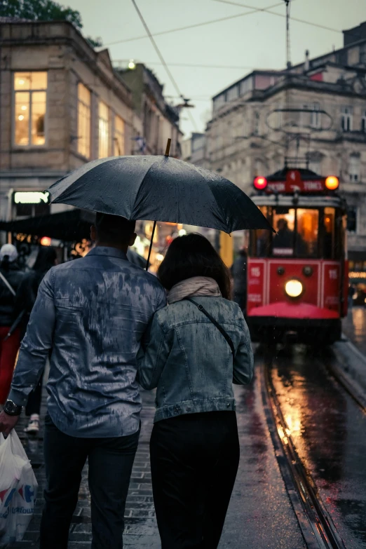 a group of people walking down a street holding umbrellas, pexels contest winner, romanticism, street tram, romantic couple, humid evening, grey