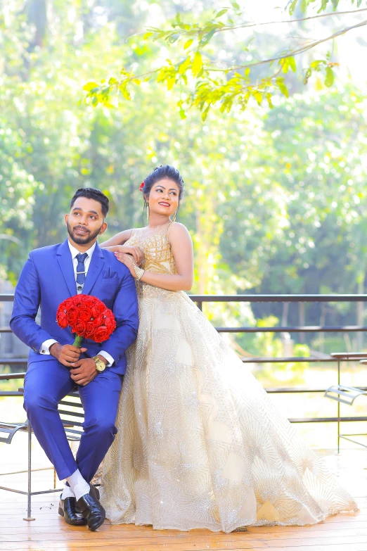 a man and a woman sitting on a bench, blue gold suit, roshan, bouquet, with backdrop of natural light