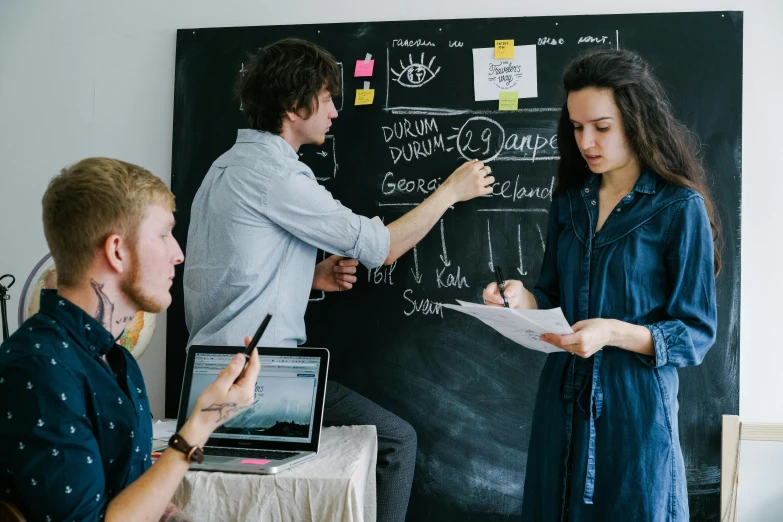 a group of people sitting around a table in front of a blackboard, by Adam Marczyński, pexels contest winner, product design, writing on a clipboard, promotional image, standing in class