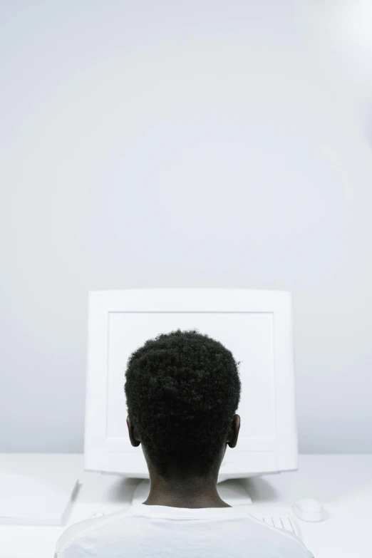 a man sitting in front of a computer monitor, a minimalist painting, inspired by Carrie Mae Weems, pexels contest winner, head and shoulders view, on a white table, back of head, square face