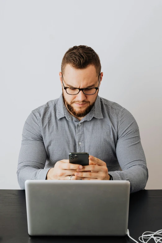 a man sitting at a table with a laptop and a cell phone, reddit post, plain background, manly face, email