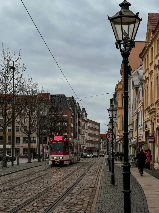 a red bus driving down a street next to tall buildings, a photo, pexels contest winner, art nouveau, in empty!!!! legnica, overcast day, detmold, fresh bakeries in the background