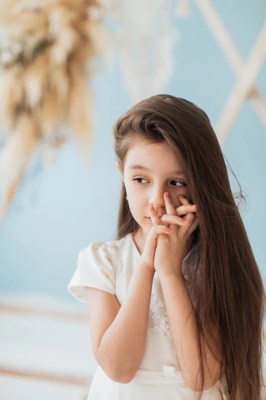 a little girl in a white dress holding her hands to her face, girl with dark brown hair, disappointed, looking off to the side, praying posture