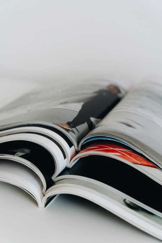 an open magazine sitting on top of a table, a picture, trending on unsplash, private press, plain background, zoomed in shots, casually dressed, sleek spines