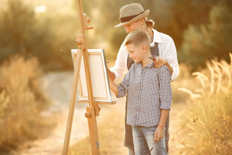 a woman standing next to a boy near a easel, inspired by artist, pexels contest winner, summer light, al fresco, guide, holding paintbrushes