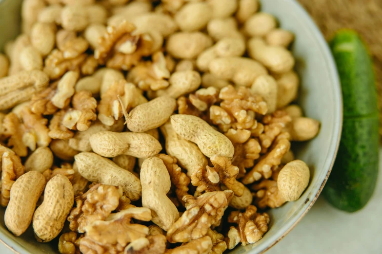 a bowl filled with nuts and a cucumber, by Julia Pishtar, trending on pexels, renaissance, peanuts, detail shot, thumbnail, walnuts