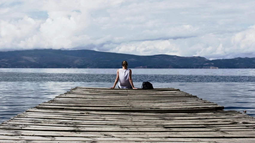 a woman sitting on a dock looking out at the water, pexels contest winner, lake baikal in the background, recovering from pain, grey, a wooden