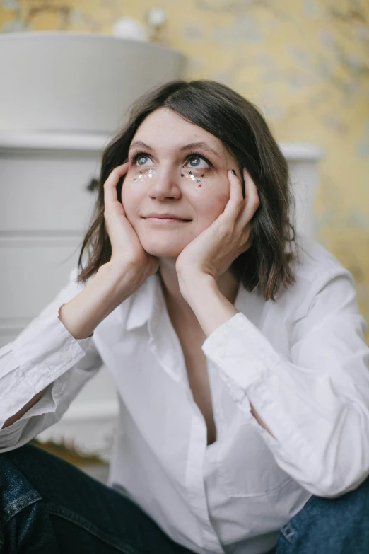 a woman sitting on the floor with her hands on her face, an album cover, inspired by Anna Füssli, gold and white eyes, happy eyes, rainny, on a pale background