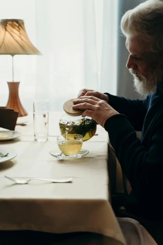 a man sitting at a table with a glass of wine, green tea, bjørn skalldrasson, grandfatherly, plating