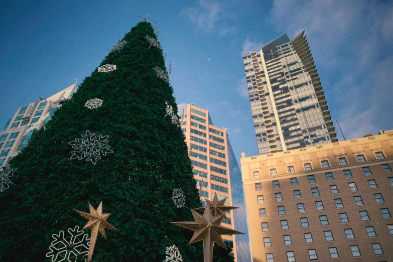 a christmas tree is set up against the sky in front of tall buildings