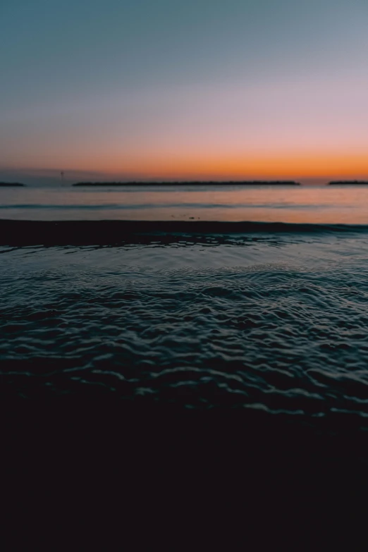 the sun is setting over a body of water, unsplash, minimalism, wavy water, 4 k cinematic still, shore, long view