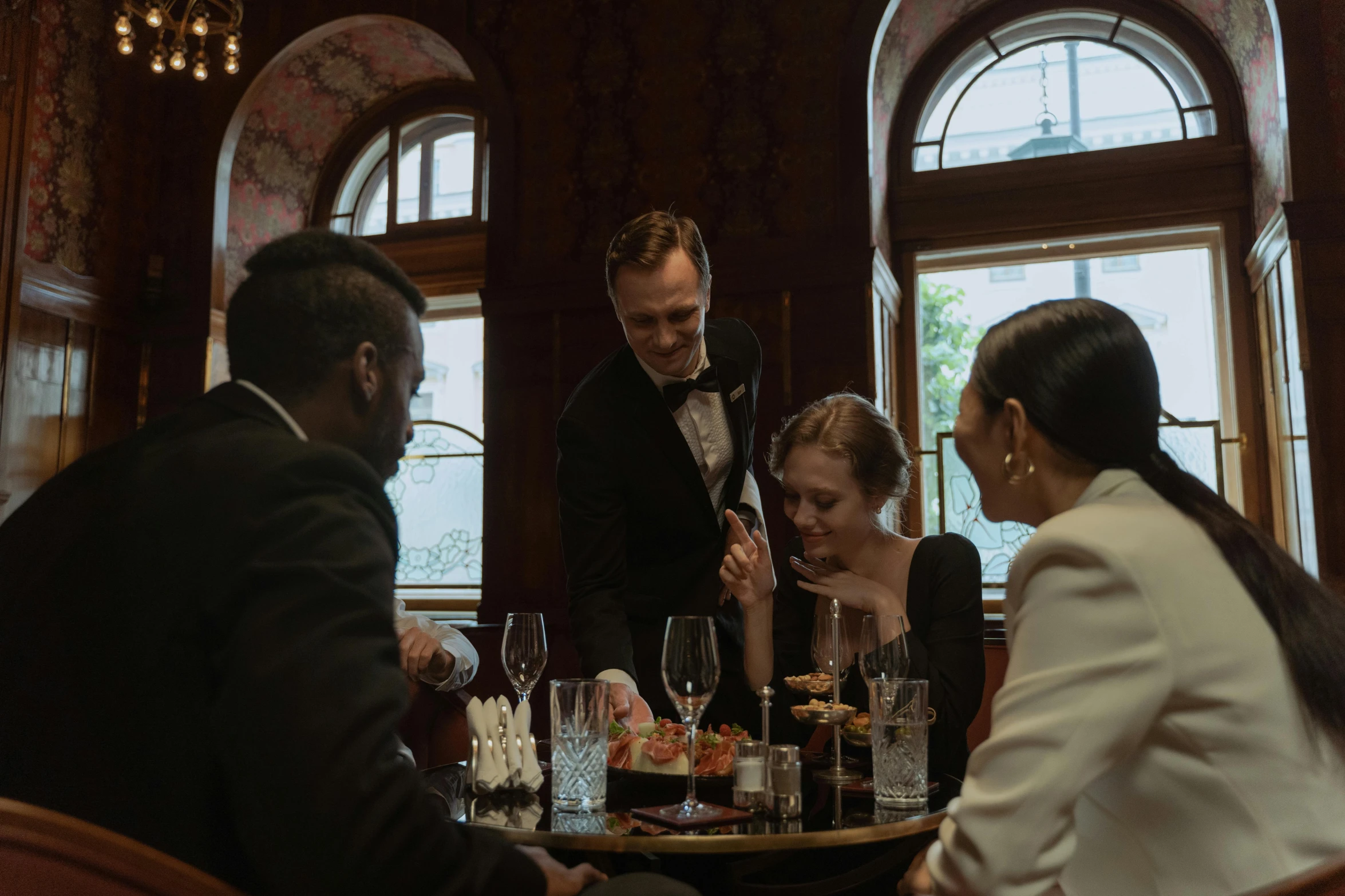 a group of people sitting around a table, luxurious environment, award winning cinematic, dapper, offering a plate of food