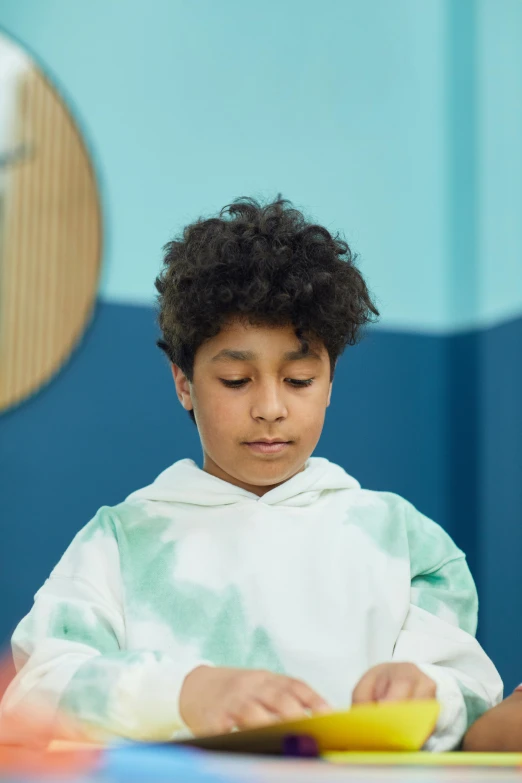 a little boy that is sitting at a table, meditating, wearing a hoodie and sweatpants, ameera al taweel, teal color graded