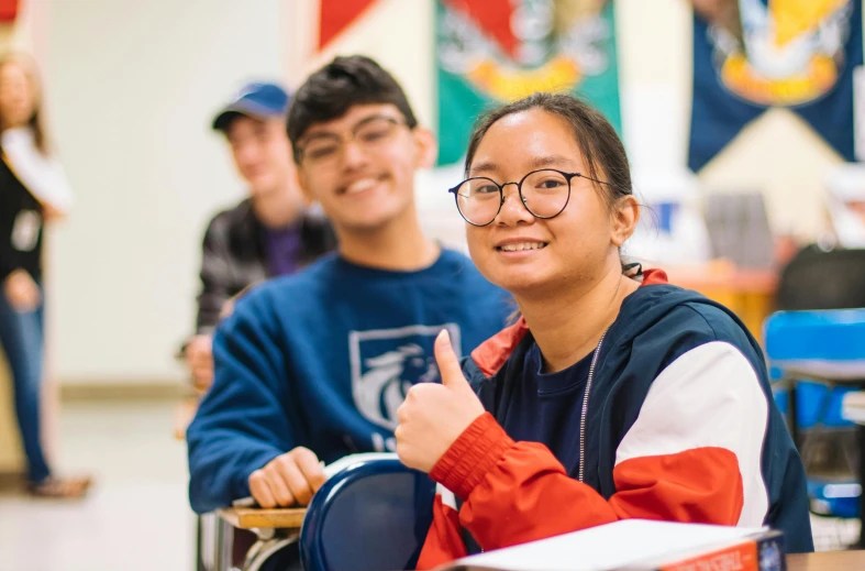 a group of students sitting at desks in a classroom, a photo, by Sam Dillemans, academic art, doing a thumb up, joy ang, smiling spartan, looking to the side off camera