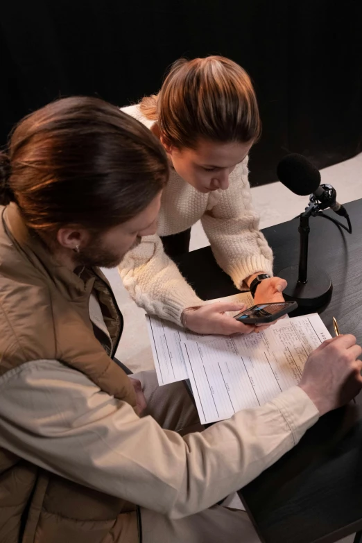 a man and a woman sitting in front of a microphone, pexels contest winner, private press, scanning items with smartphone, female investigator, papers on table, studio lit