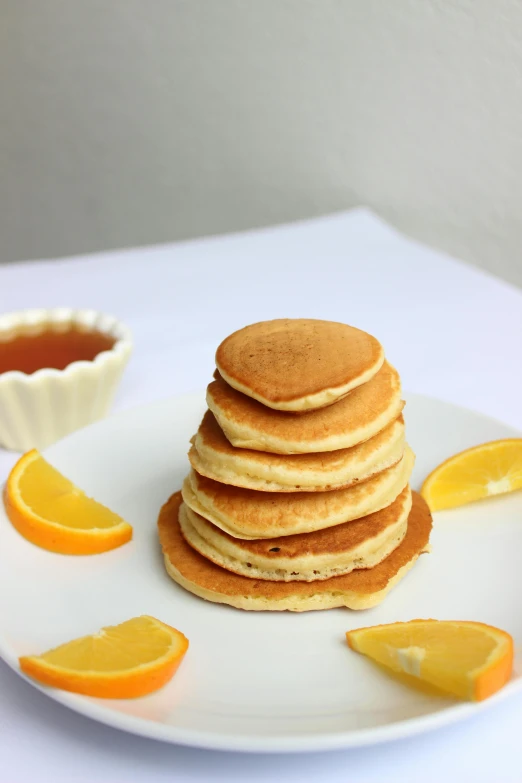 stack of pancake cut with slices and orange segments on white plate