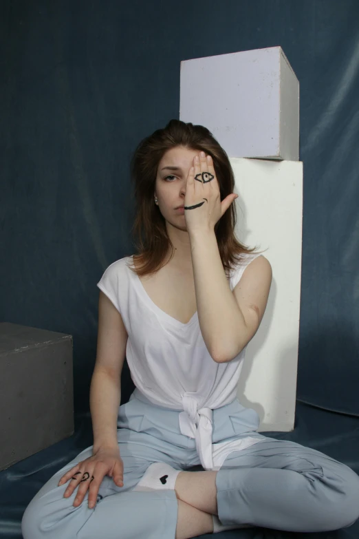 a woman sitting on the ground in front of a refrigerator, an album cover, inspired by Hannah Frank, white prosthetic eyes, in a photo studio, on a gray background, portrait of a female art student