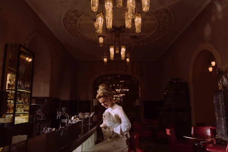 the woman is standing by a bar with lights hanging overhead