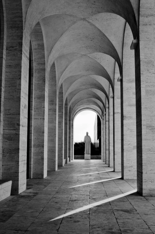 a black and white photo of the inside of a building, inspired by Pierre Pellegrini, white stone arches, figure in center, mausoleum, peter eisenman