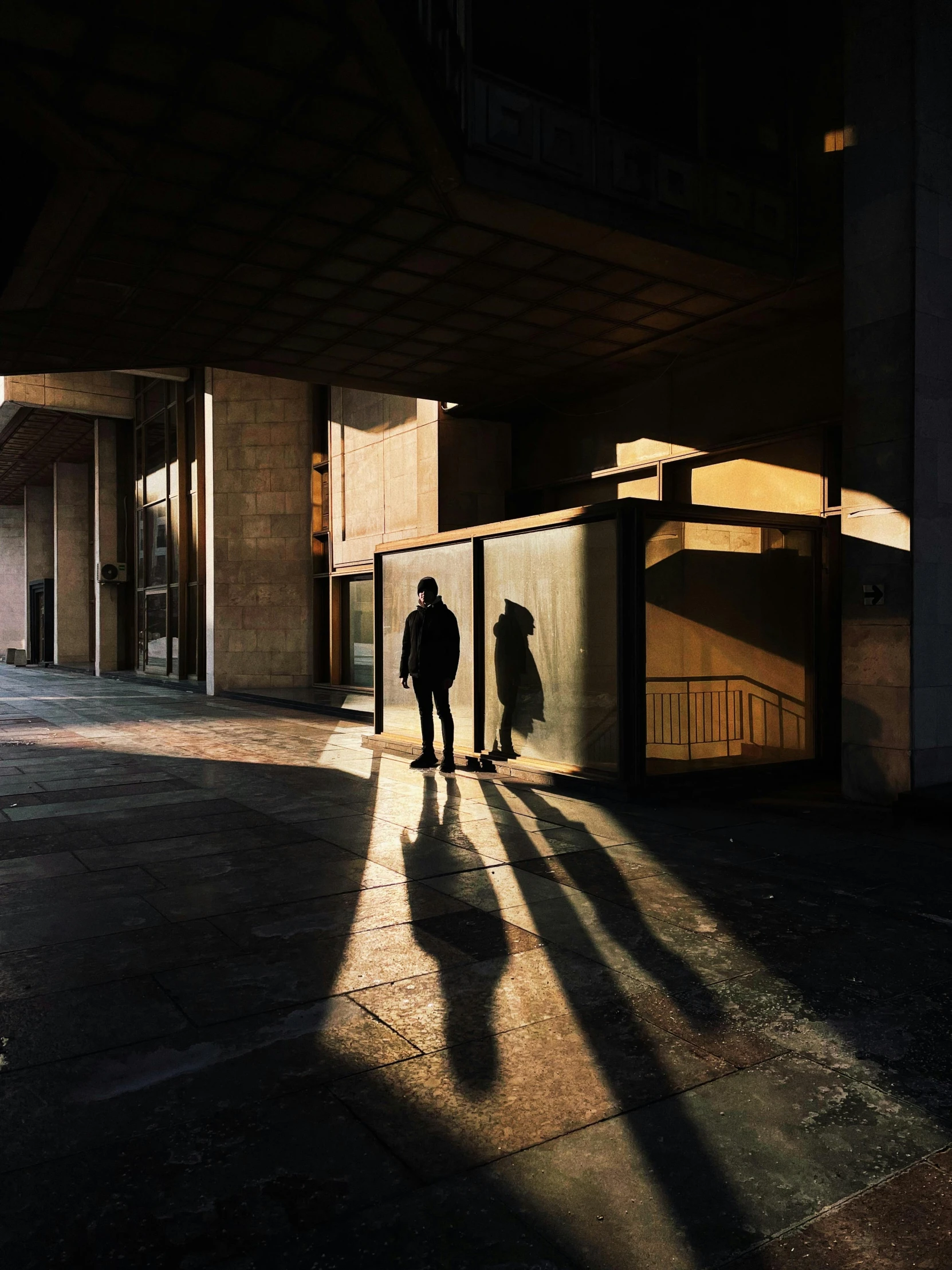 a couple of people that are standing in a building, a photo, unsplash contest winner, brutalism, long shadows, dark city bus stop, ignant, shafts of sunlight in the centre